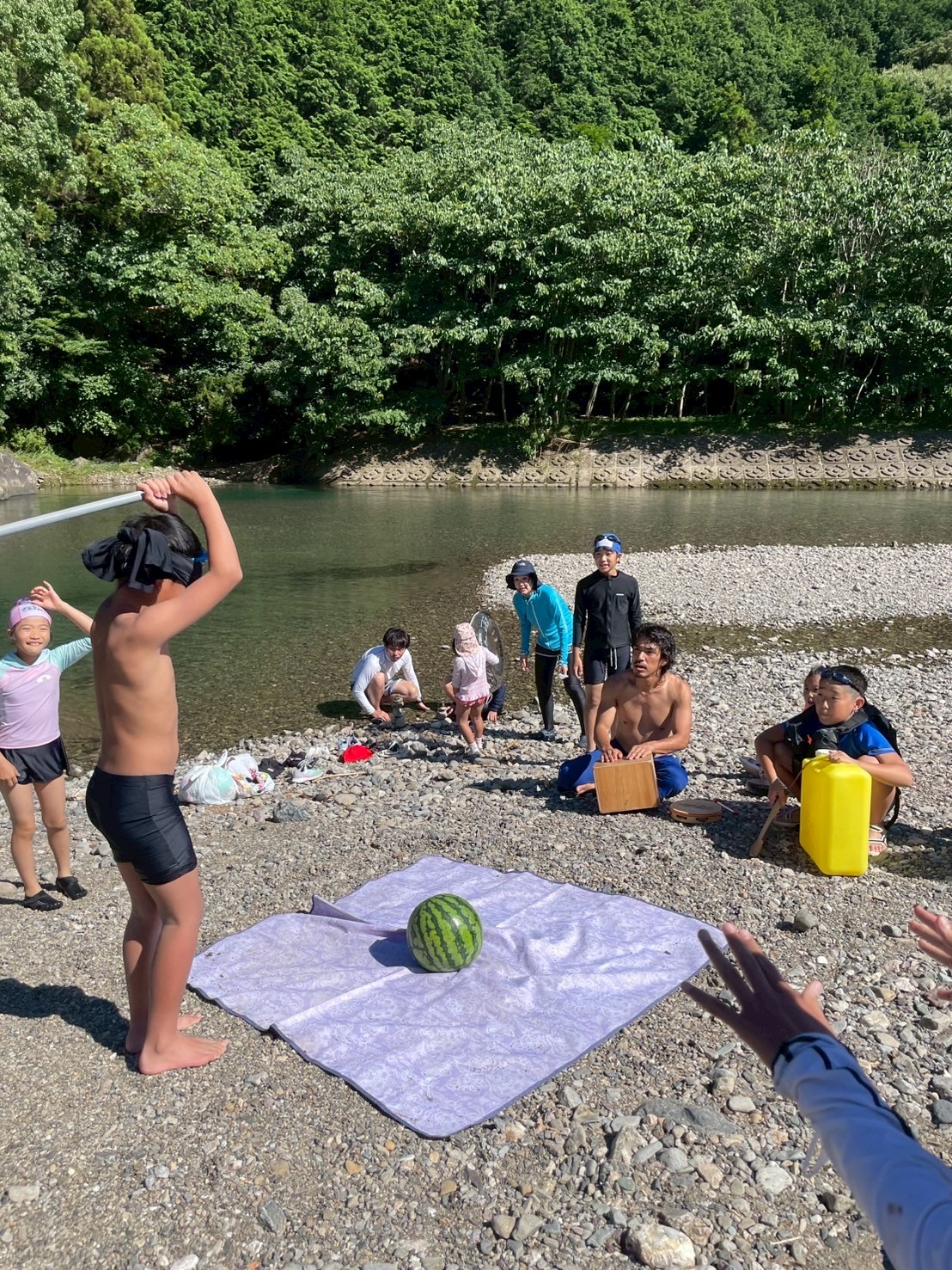 川辺でスイカ割りを楽しむ伊勢志摩リトリートの参加者